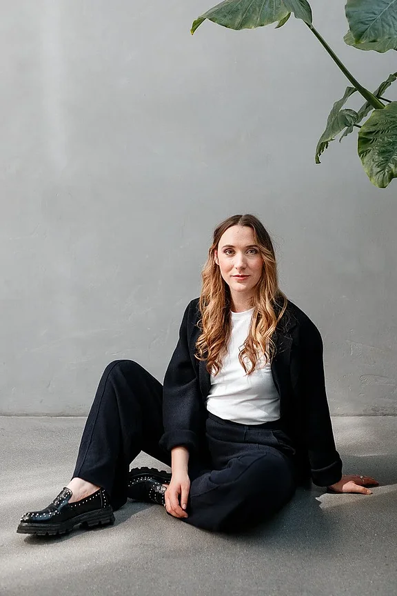 Personal-Branding.Business-Portrait einer Frau: Sie trägt einen dunkelblauen Blazer mit einem weißen Shirt, hat schulterlanges blondes Haar und lächelt freundlich vor einem hellgrauen Hintergrund.