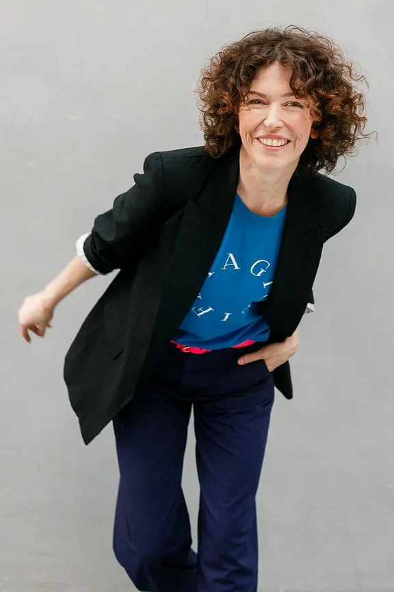 Eine Frau in professioneller Business-Kleidung posiert für ein Porträt. Sie trägt einen gut sitzenden Blazer in neutralen Farben und lächelt dezent in die Kamera. Der Hintergrund ist weich und unscharf, um den Fokus auf die Frau zu legen. Dieses Bild