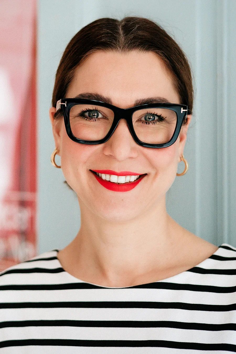 Stefanie Heiserowski mit schwarzer Brille, rotem Lippenstift und gestreiftem Oberteil lächelt in die Kamera