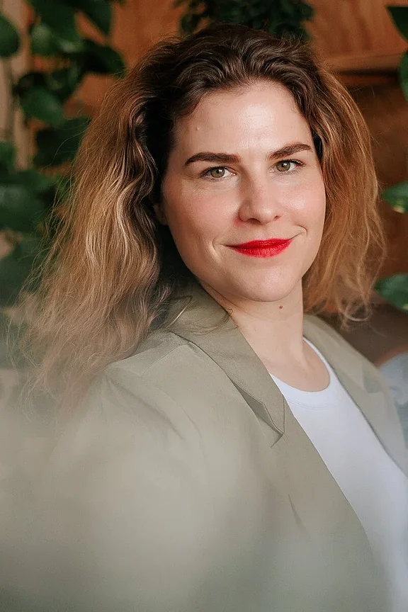 Business-Portrait einer Frau in professioneller Kleidung: Sie trägt ein elegantes, hellblaues Oberteil, lächelt freundlich und steht vor einem dezenten, grauen Hintergrund für Personal Branding Fotografie