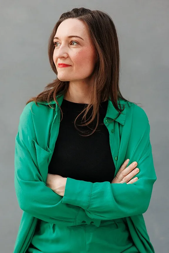 Business-Branding-Portrait einer Frau: Sie trägt einen schwarzen Blazer und ein weißes Oberteil, schaut freundlich in die Kamera und sitzt vor einem neutralen, grauen Hintergrund