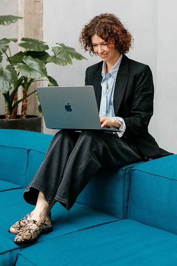 Personal Branding Business-Portrait einer Frau in formeller Kleidung: Sie trägt einen dunkelblauen Blazer und ein weißes Hemd, schaut freundlich in die Kamera und sitzt vor einem neutralen, grauen Hintergrund.